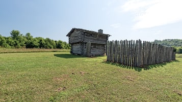A rustic log cabin with a wooden fence in a grassy field.