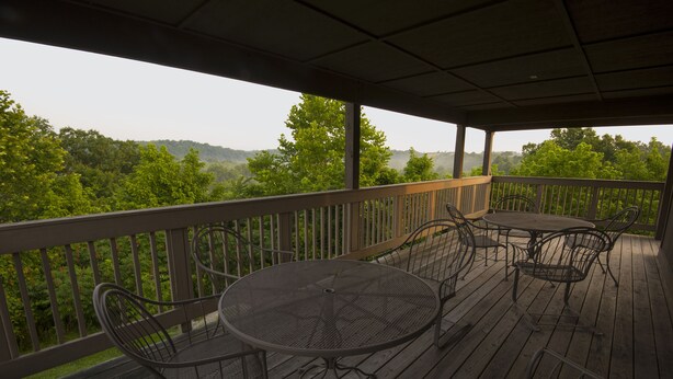 A covered outdoor deck with a table and chairs, overlooking a forested area.