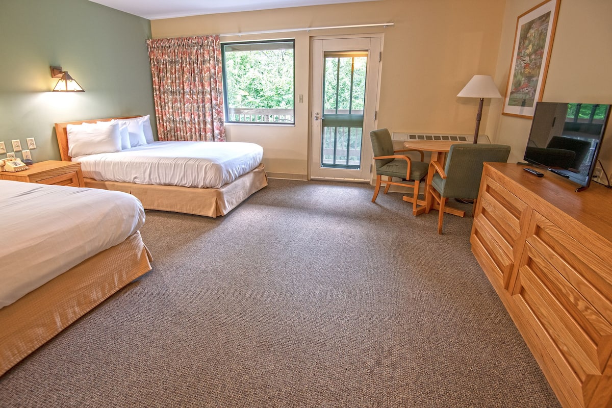A hotel room with two beds, a desk, a chair, a television, and a door leading to a balcony.