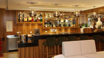 Zona bar con rivestimenti in legno, un bancone nero e diversi sgabelli da bar.