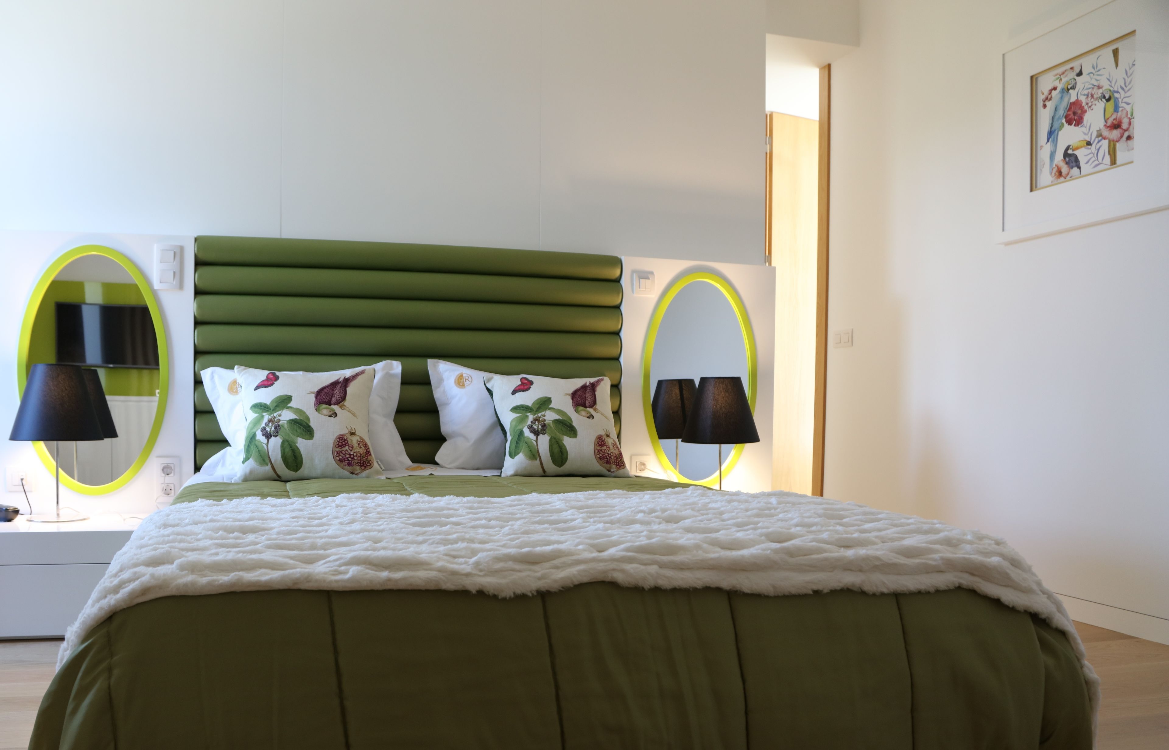 A neatly arranged bedroom with a green upholstered headboard, a white fluffy bedspread, and two bedside lamps with black shades.
