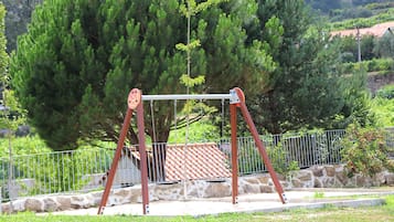 Une balançoire dans un parc, avec un mur de pierre et une clôture métallique en arrière-plan.