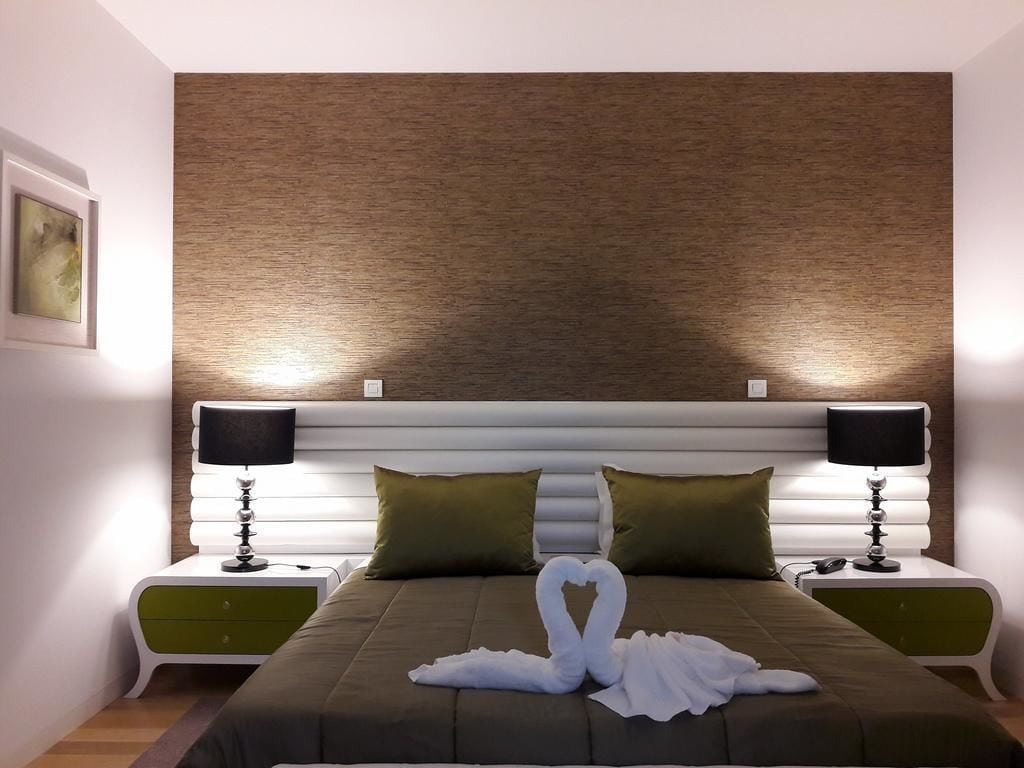 A modern hotel room with a large bed, two nightstands, and a wall-mounted headboard.