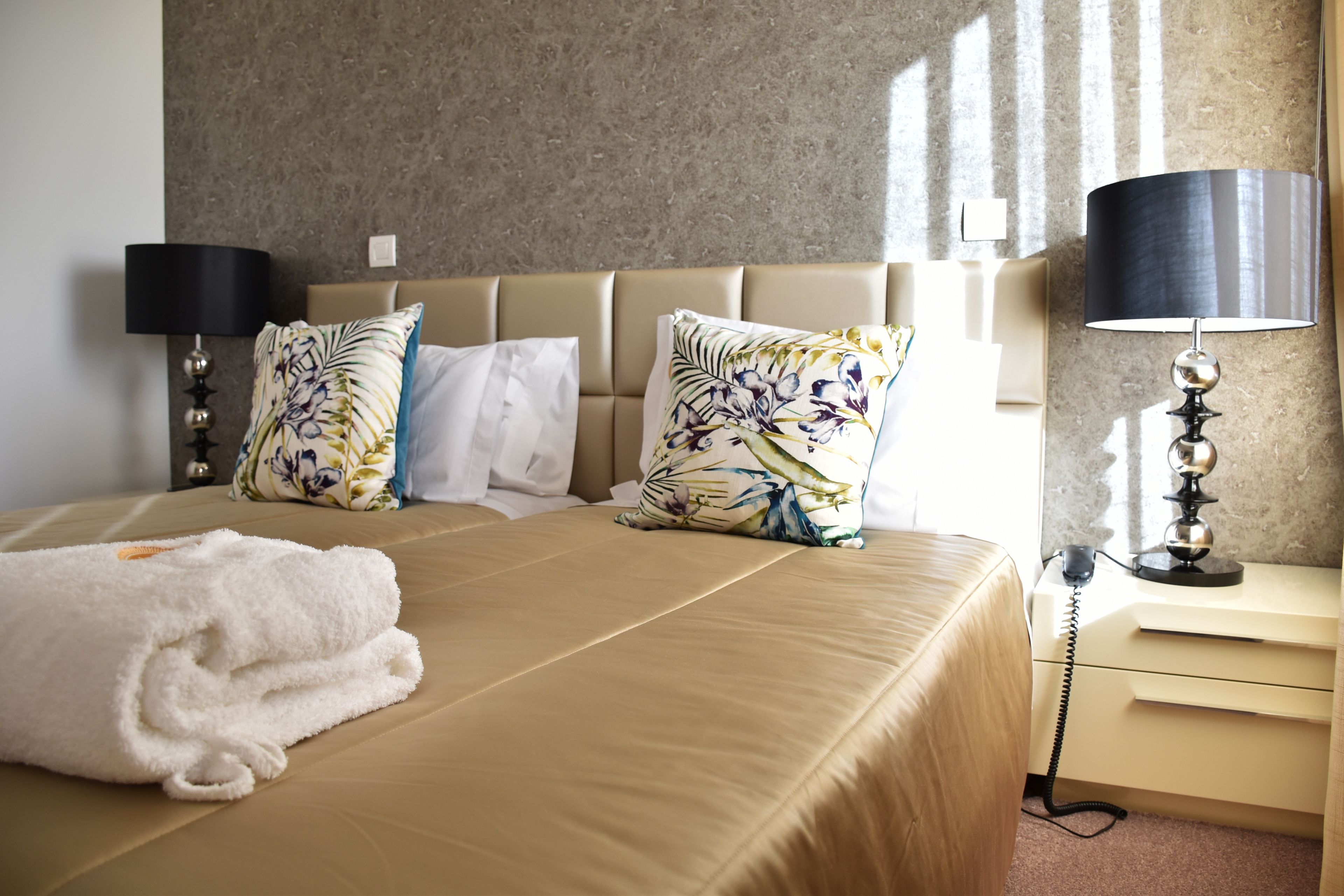 Habitación de hotel con cama, dos almohadas, lámpara de noche, mesita de noche y teléfono.
