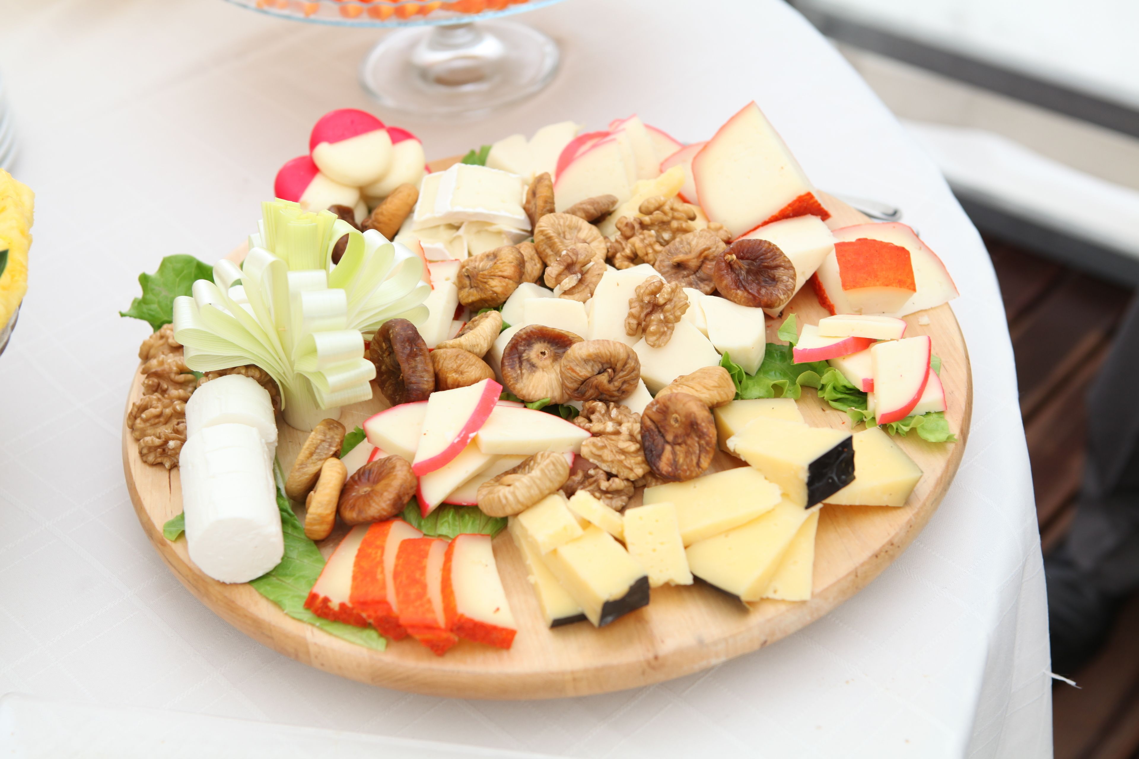 A wooden platter with assorted fruits and nuts, including apples, walnuts, and cheese, on a white tablecloth.