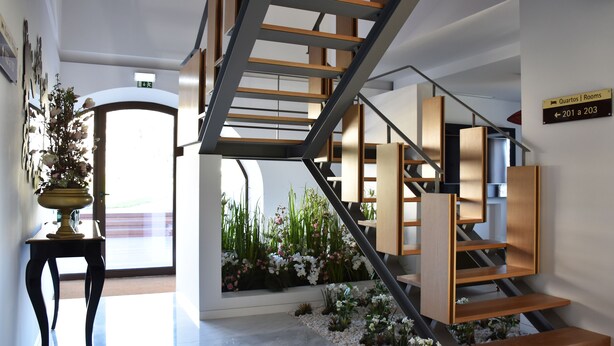 Un interior moderno con una escalera, una planta en maceta y un cartel que indica las habitaciones 201 a 203.
