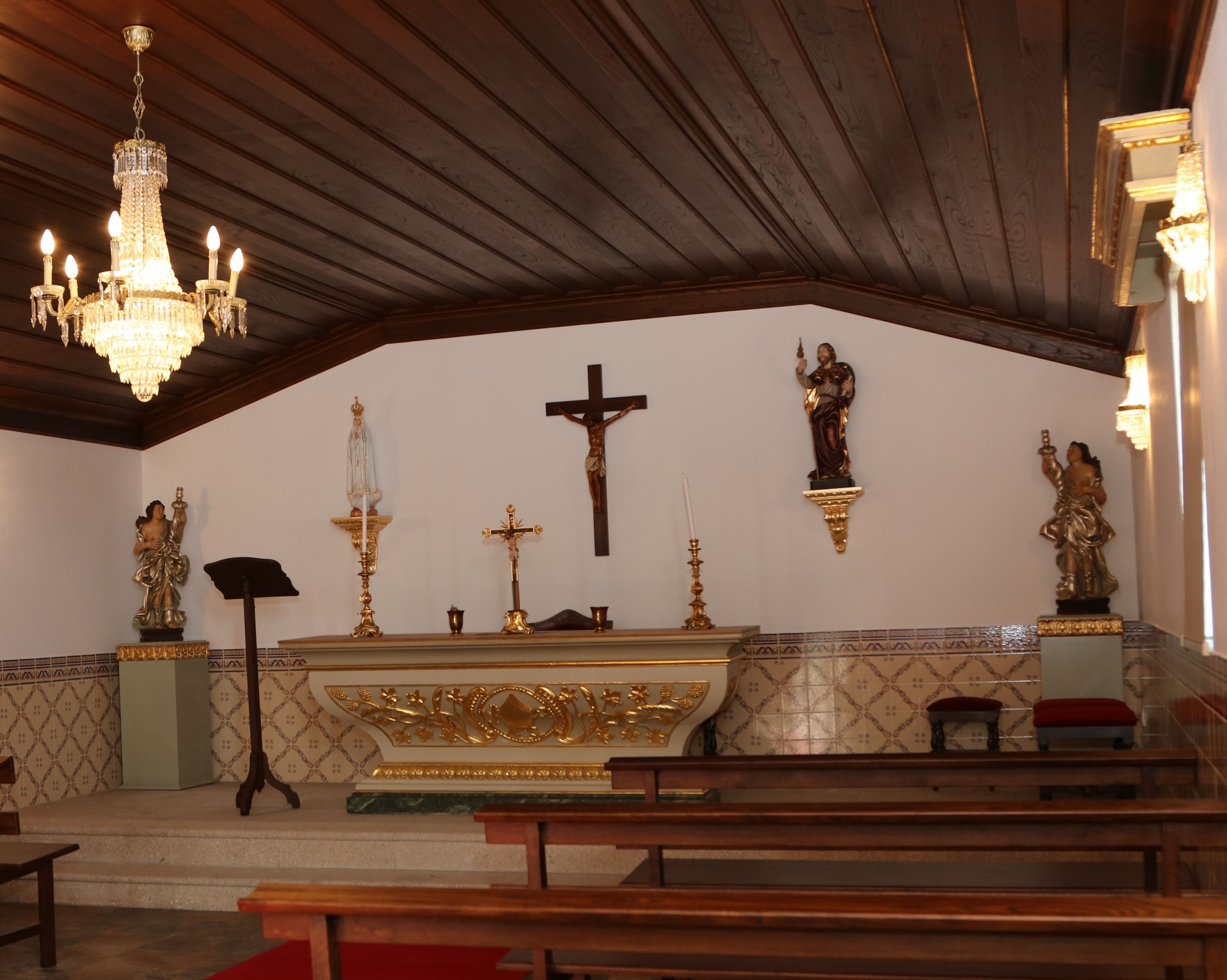 A church interior with a wooden ceiling, a chandelier, a cross, and statues.