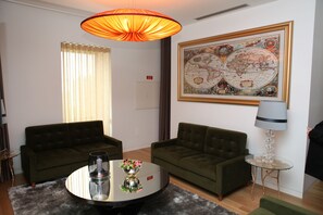 A modern living room with two green sofas, a round coffee table with a vase, a globe map on the wall, and a floor lamp. - Hotel Rural Quinta das Quintães (Penafiel)