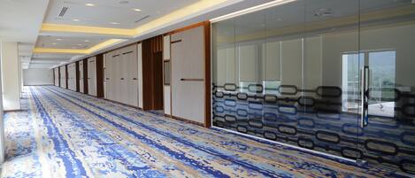 A long corridor with patterned carpet, glass partitions, and doors leading to rooms.