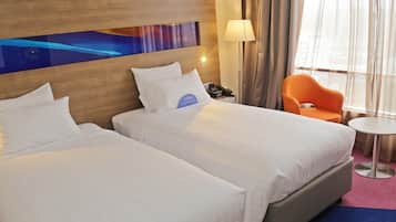 A hotel room with two beds, a nightstand with a lamp, an orange chair, and a small table.