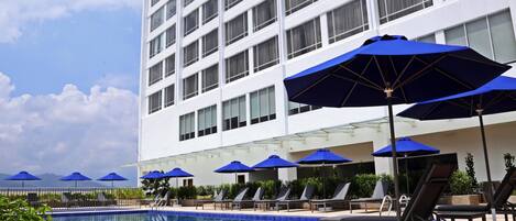 Un hôtel doté d’une piscine, de parasols bleus et de chaises longues.
