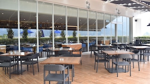Ein Außenbereich eines Cafés mit Tischen, Stühlen, großen Fenstern und Blick ins Freie.
