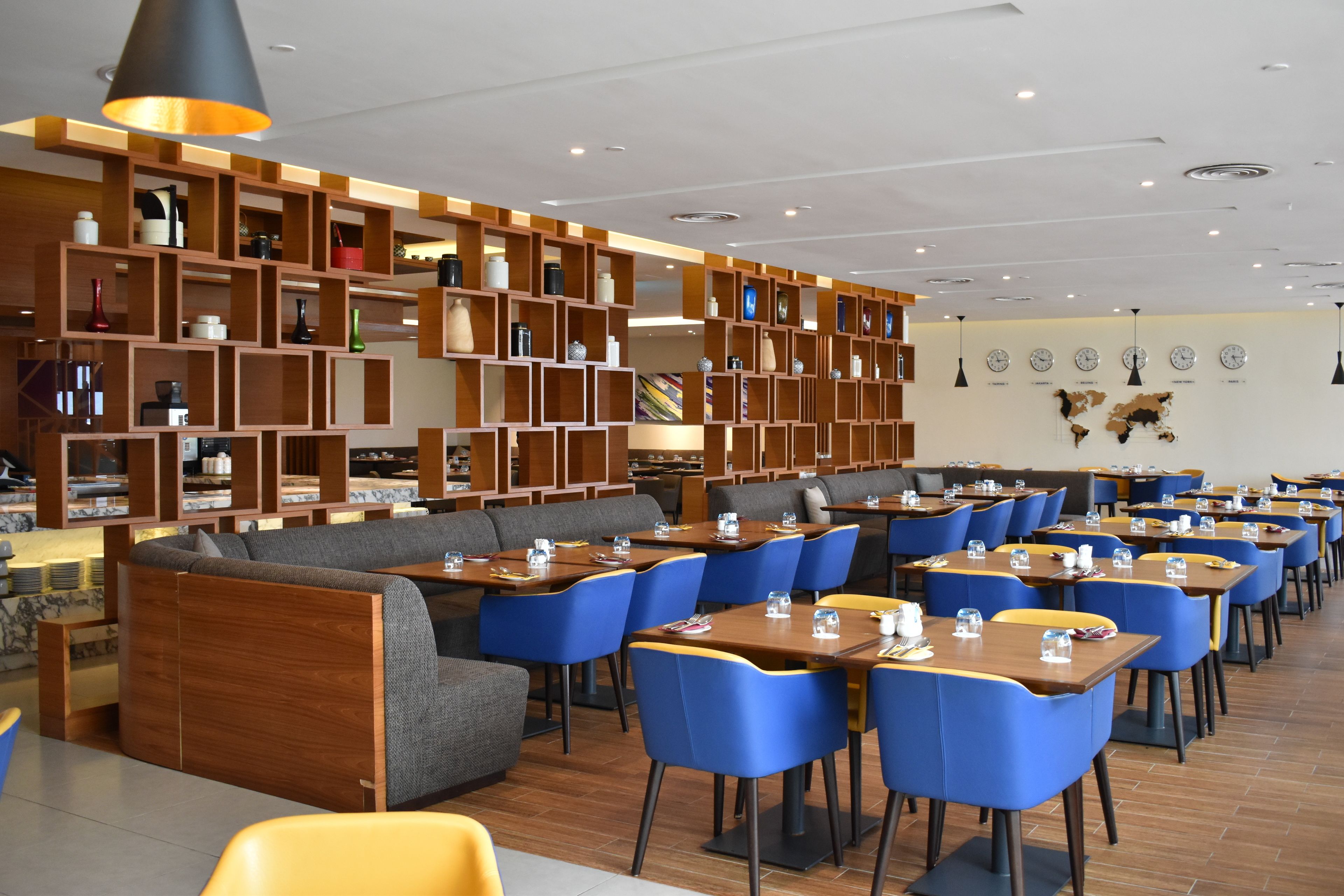 A modern restaurant with wooden shelving displaying various items, blue chairs, and tables arranged for dining.