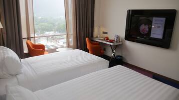 A hotel room with two beds, a desk with a computer, a chair, and a TV displaying a promotional message.