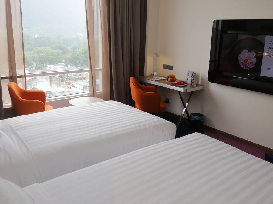 A hotel room with two beds, a desk with a computer, a chair, and a TV displaying a promotional message.
