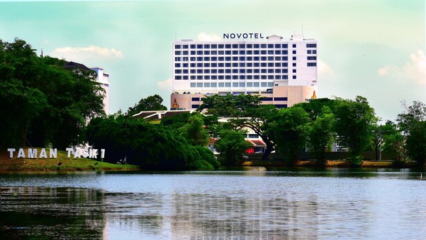 Ein Novotel Hotel mit Blick auf einen See und umliegende Grünflächen.