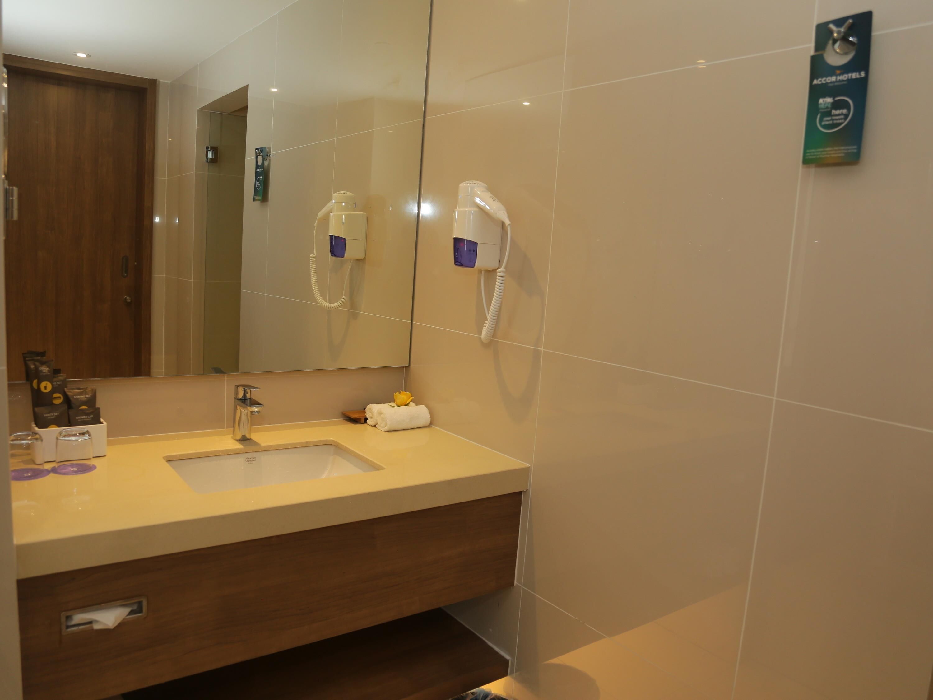 A modern bathroom with a large mirror, two hair dryers mounted on the wall, a sink, and a towel rack.