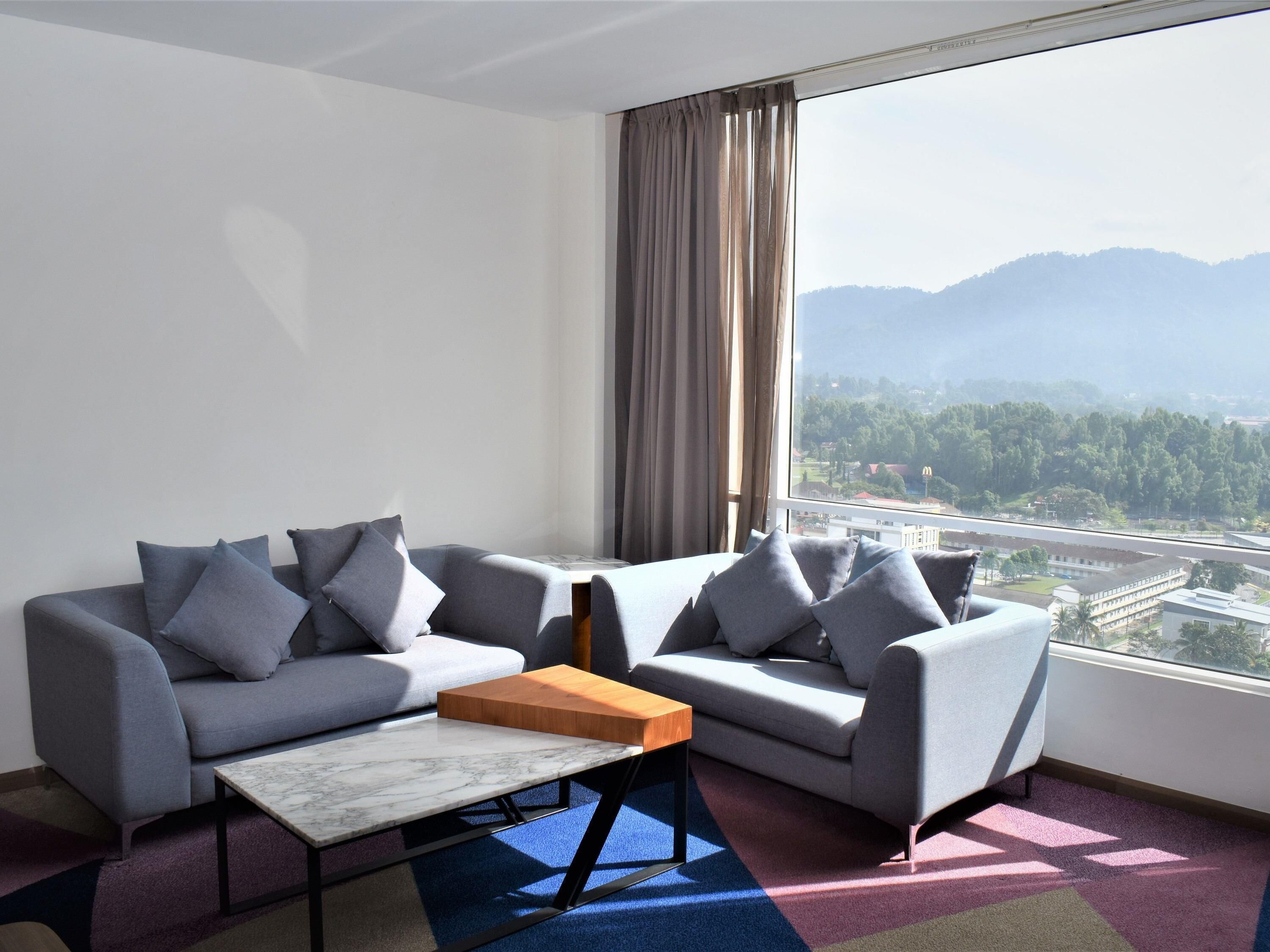 A modern hotel room with a sofa set, a coffee table, and a large window offering a mountain view.