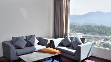 A modern hotel room with a sofa set, a coffee table, and a large window offering a mountain view.