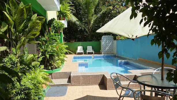 A swimming pool with a tiled deck, surrounded by lush greenery and two white lounge chairs. - Panama Canal Inn (Panama City)