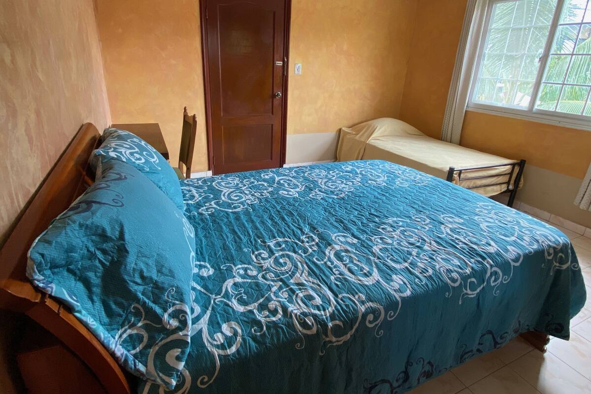A bedroom with a bed, a small table, a chair, a door, and a window.