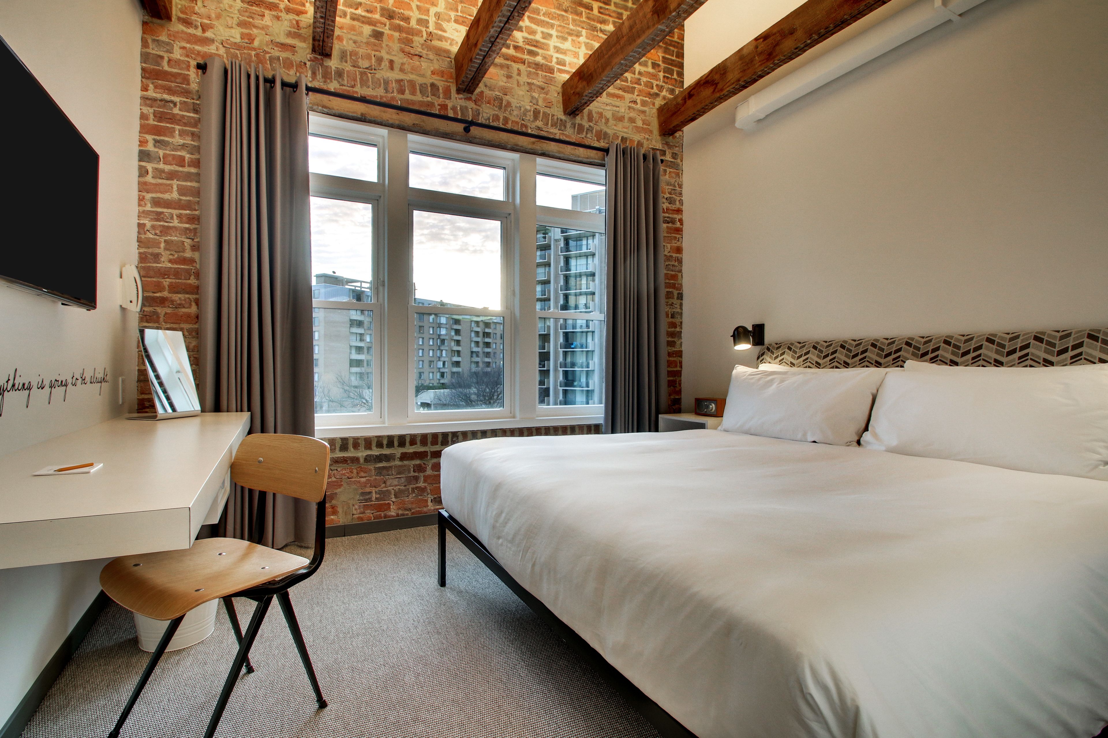 A hotel room with a bed, a desk, a chair, and a window with curtains.