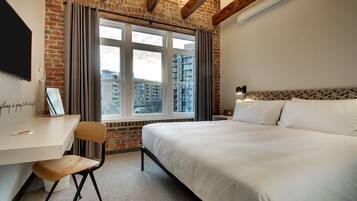 A hotel room with a bed, a desk, a chair, and a window with curtains.