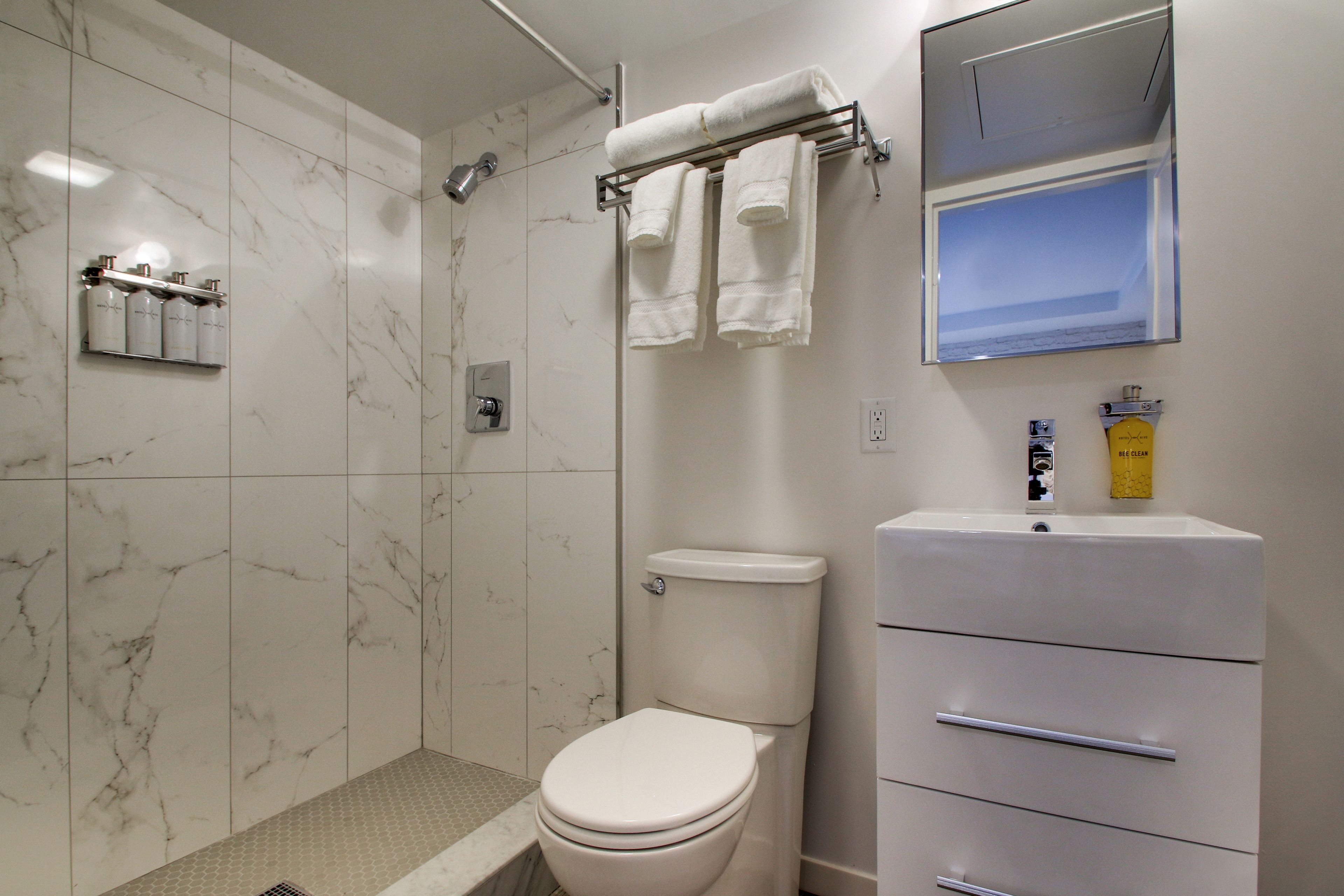 A bathroom with a toilet, a shower, a sink, and a mirror.