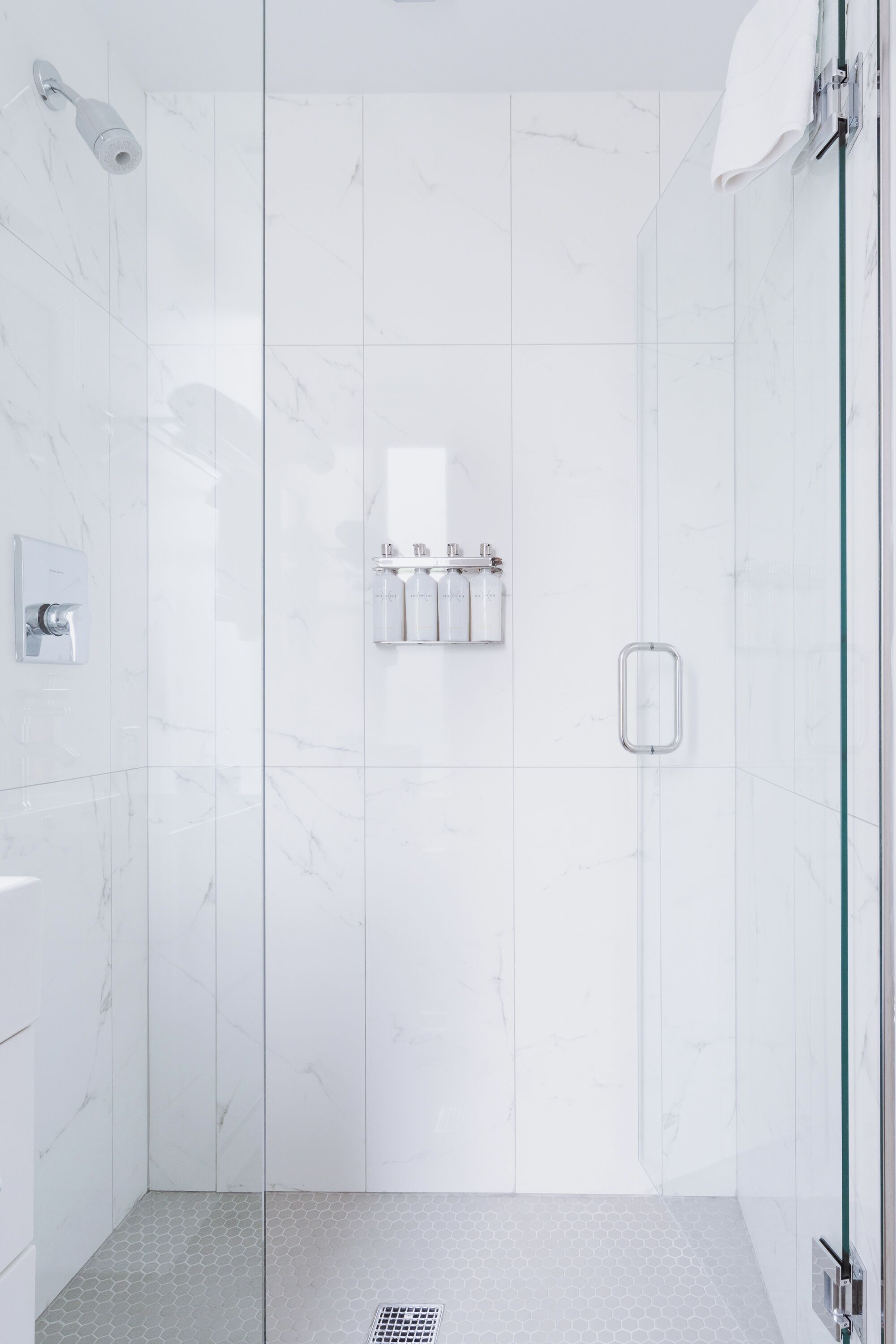 A modern shower with glass doors, a control panel, and a shelf with toiletries.