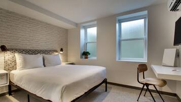A bedroom with a bed, a desk, a chair, a potted plant, and a window.