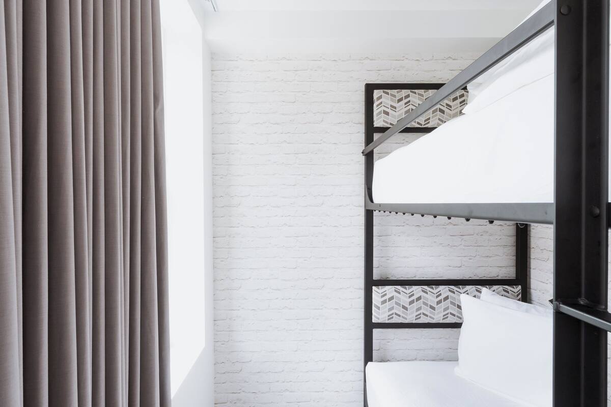 A bunk bed with a white mattress and patterned headboard, against a white brick wall.
