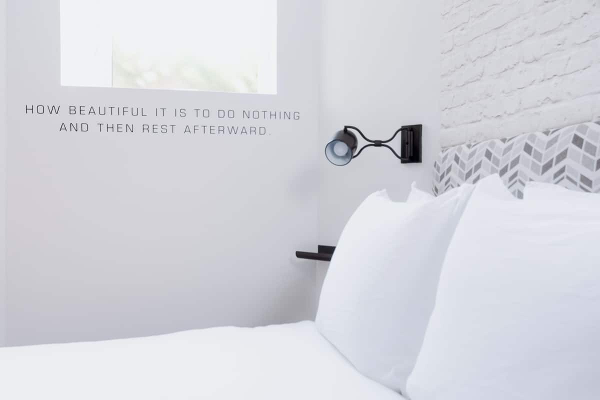 A minimalist hotel room with a bed, a wall-mounted reading light, and a decorative wall panel.