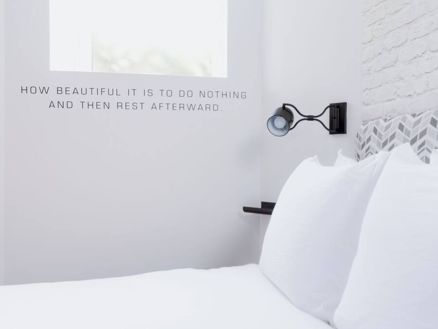 Habitación de hotel minimalista con cama, lámpara de lectura fijada a la pared y un panel decorativo.