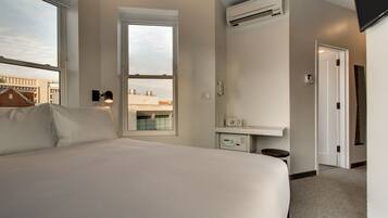 A hotel room with a large bed, a window, an air conditioning unit, a bedside table, and a small table with a radio.