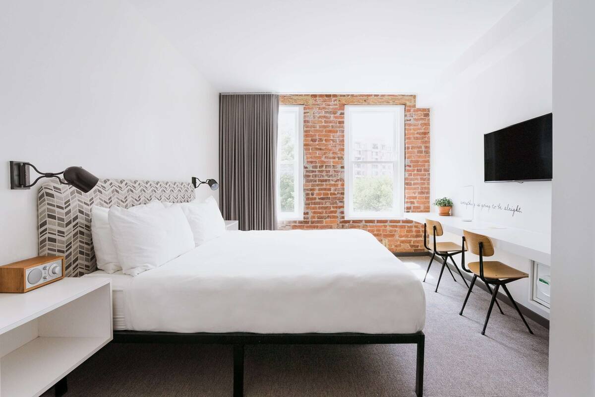 A modern hotel room with a bed, a desk, and a TV.