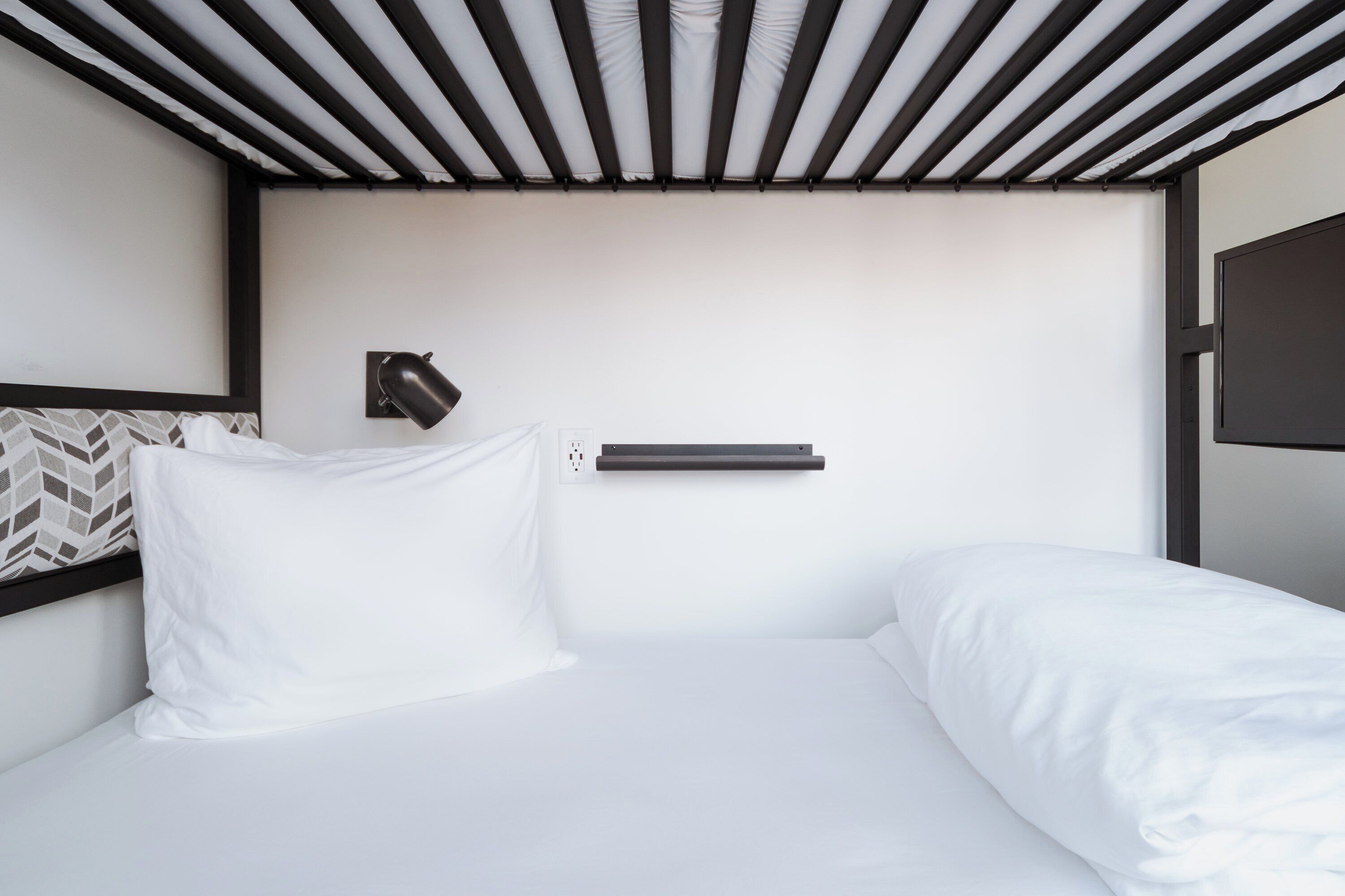 A modern hotel room with a bed, a wall-mounted lamp, and a power outlet.