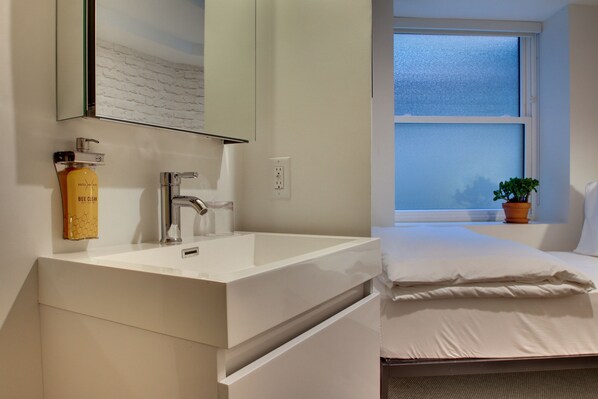 Un baño moderno con un lavamanos blanco, un espejo y una ventana con vistas al cielo.