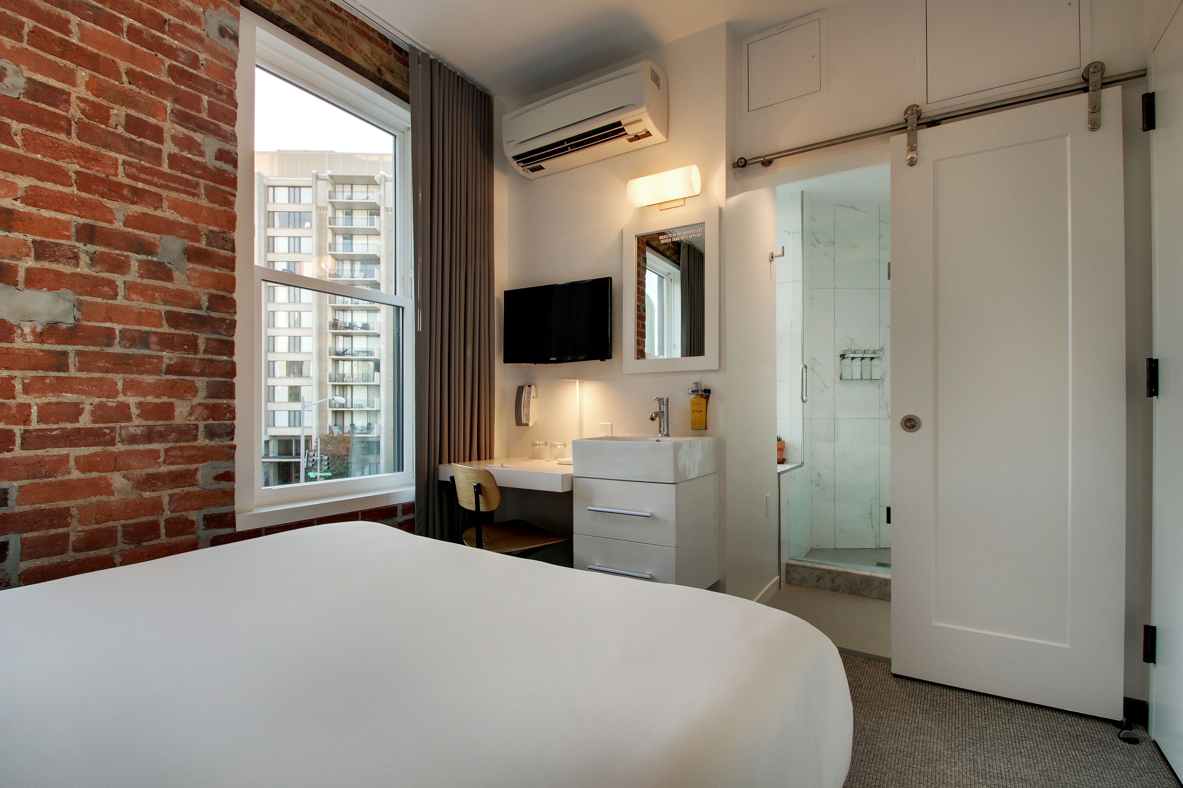 A hotel room with a large bed, a desk with a chair, a bathroom with a shower, and a TV mounted on the wall.