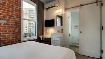 A hotel room with a large bed, a desk with a chair, a bathroom with a shower, and a TV mounted on the wall.