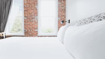 A bedroom with a brick wall, a large window, and a bed with white bedding.