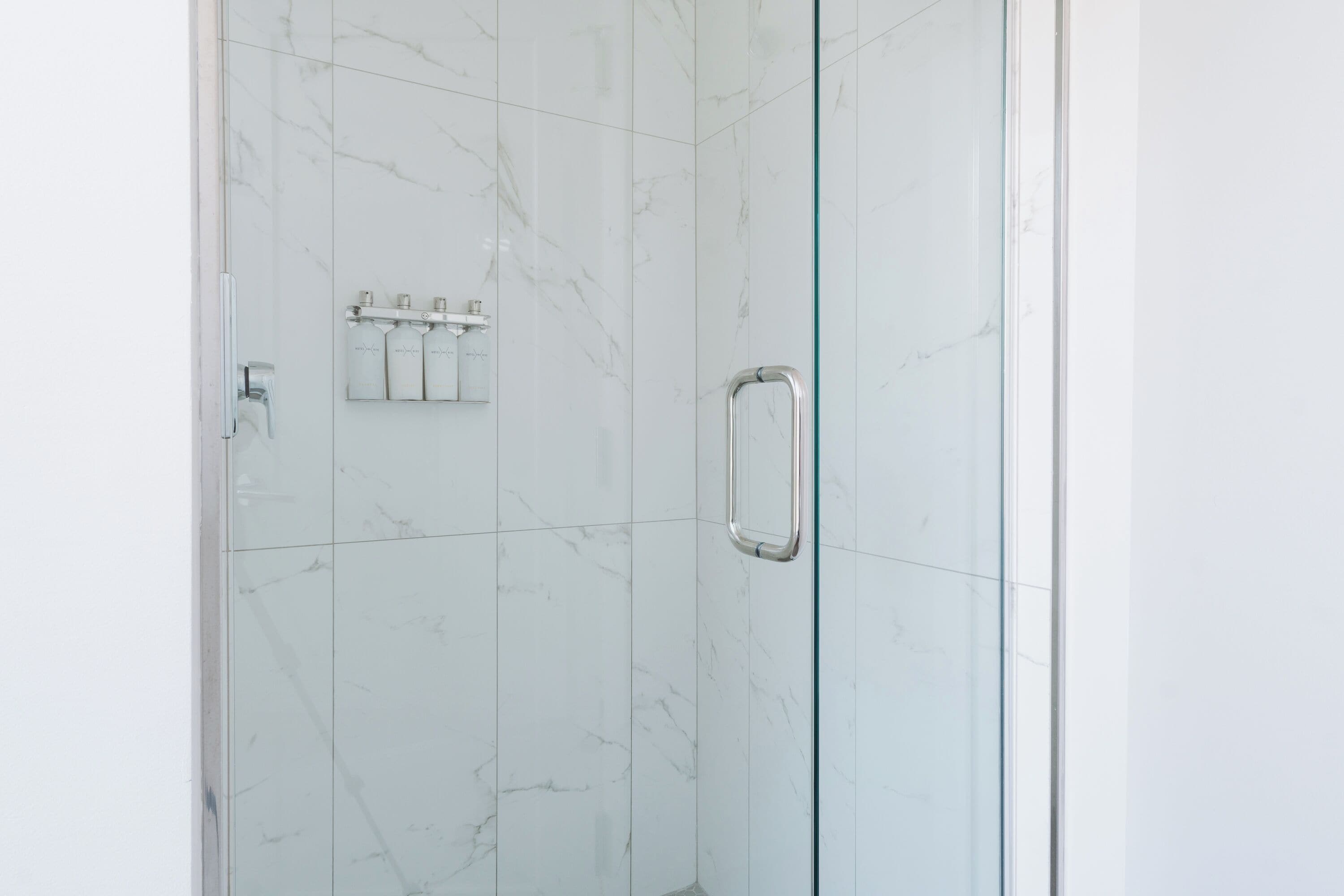 Une douche entièrementClose avec des carreaux de marbre blanc et une poignée en chrome.