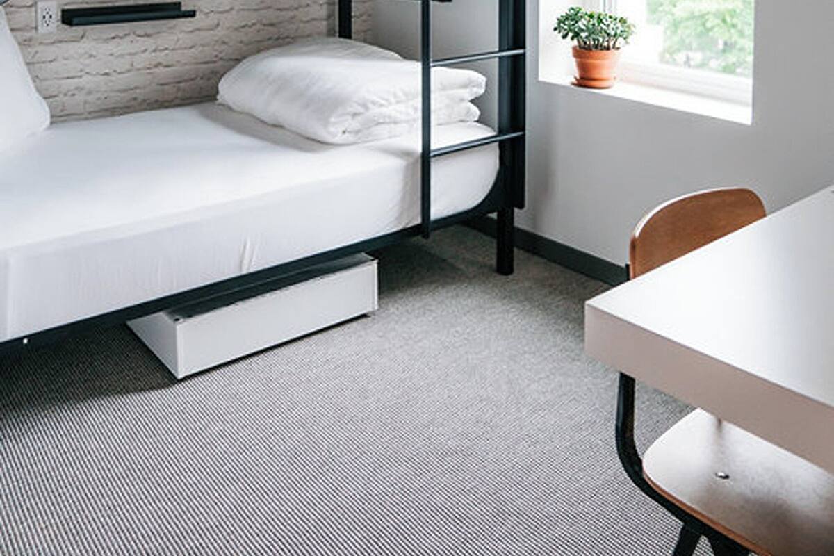 A bunk bed with a TV above it, a small table, and a window with a plant.