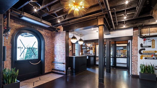 A modern interior with exposed brick walls, a black reception desk, and directional signage for amenities like food, restrooms, and a hive bar. - Hotel Hive (Washington)
