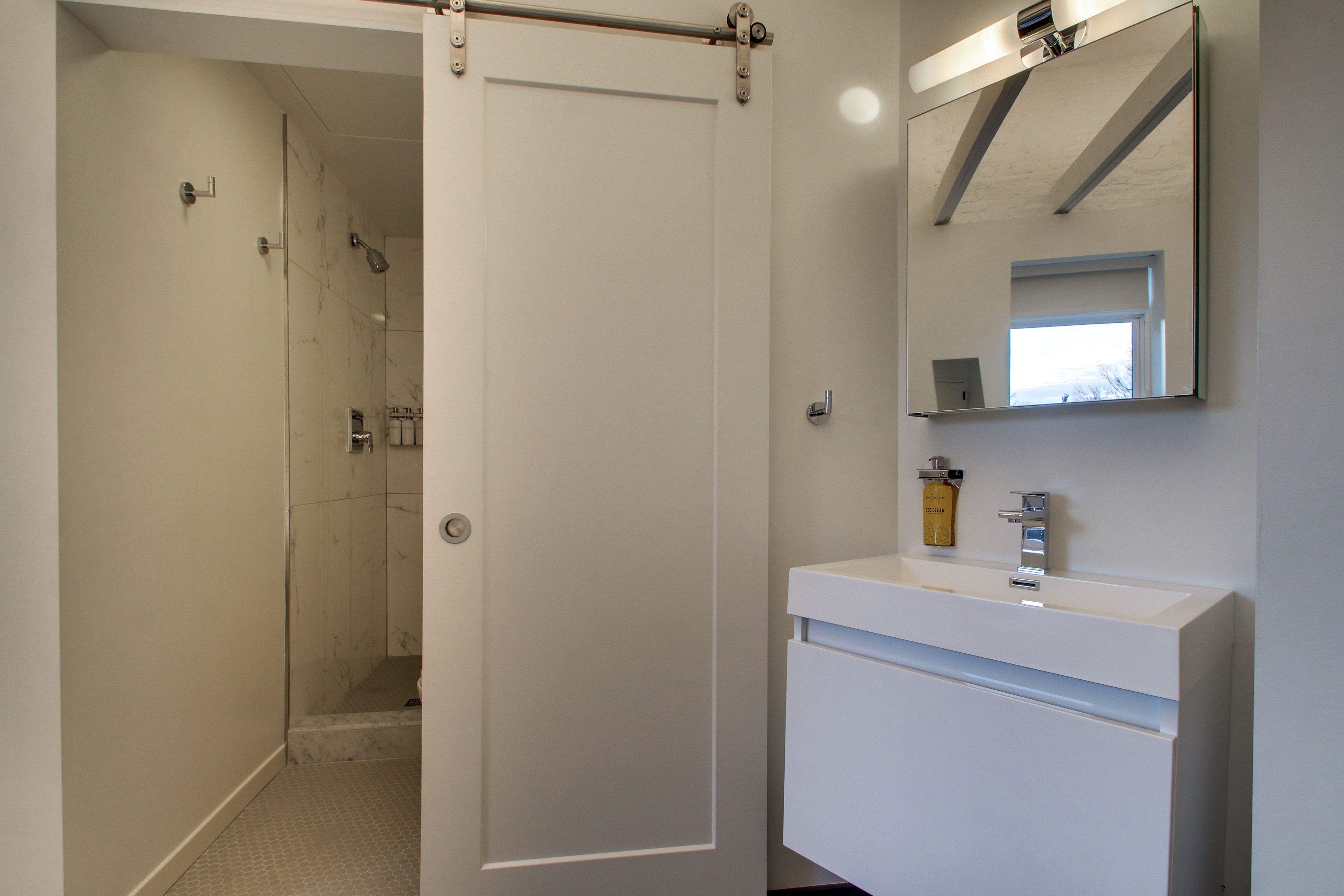 A modern bathroom with a glass shower enclosure, a white sink with a mirror above it, and a door leading to another room.