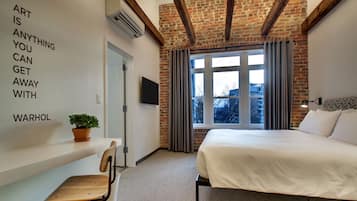 Habitación de hotel moderna con pared de ladrillo, una cama grande, televisor de pantalla plana y una cita motivacional en la pared.