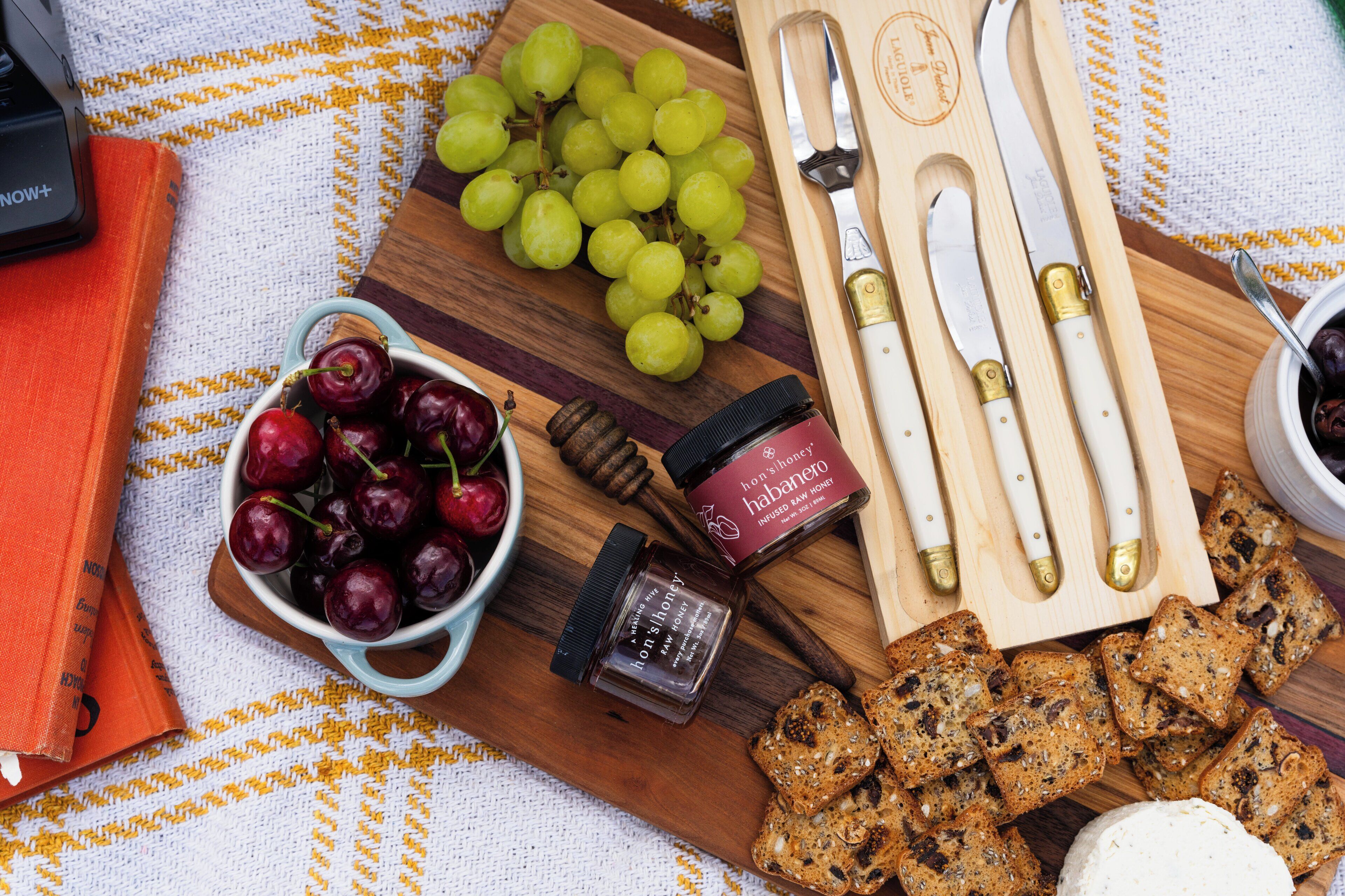 A wooden board with grapes, cherries, honey, and bread.