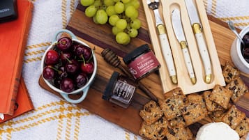 A wooden board with grapes, cherries, honey, and bread.