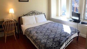 Una cama bien hecha con un edredón estampado, una lámpara de noche, una silla y un televisor sobre un alféizar.