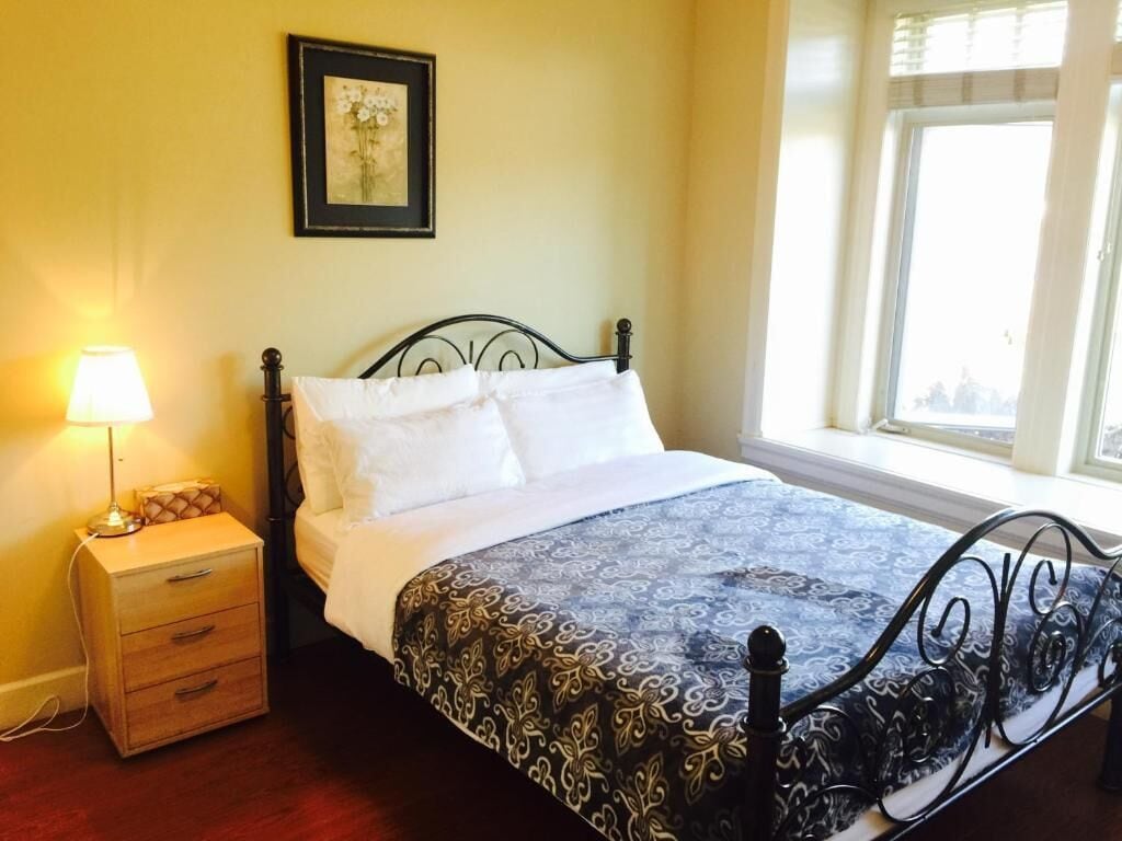 Una cama con una colcha estampada, una mesita de noche con una lámpara y una ventana con cortinas.