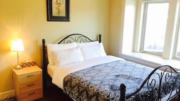 Una cama con una colcha estampada, una mesita de noche con una lámpara y una ventana con cortinas.